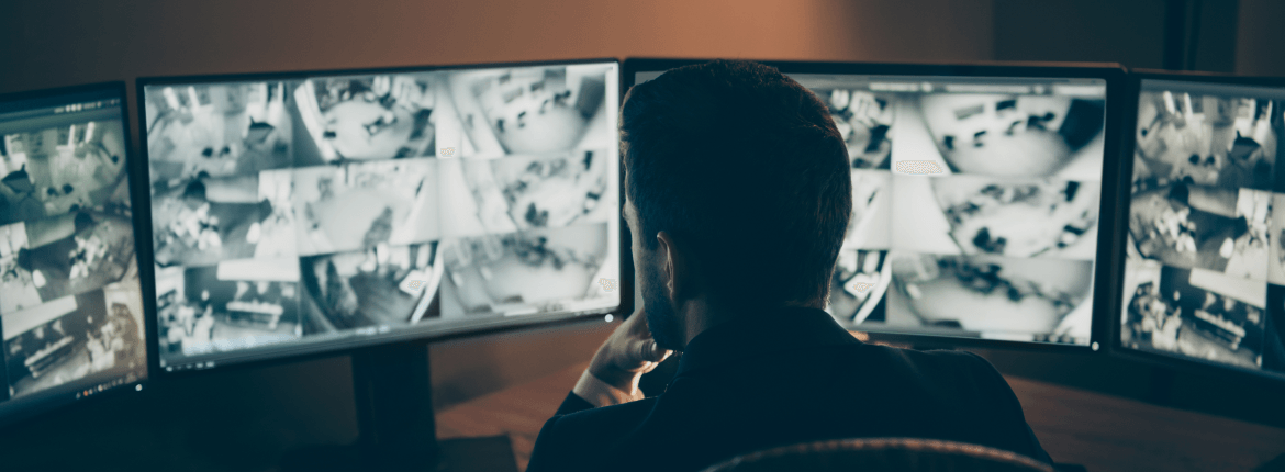 Male security agent reviewing video footage for a retail location and monitoring fraud in four screens.