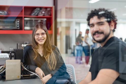 Two colleagues engaged in discussion while seated at a table in a modern office environment.