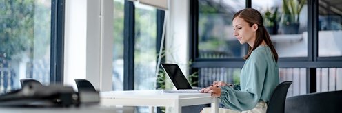 Millenial female worker reviewing notes and utilizing a computer in an office