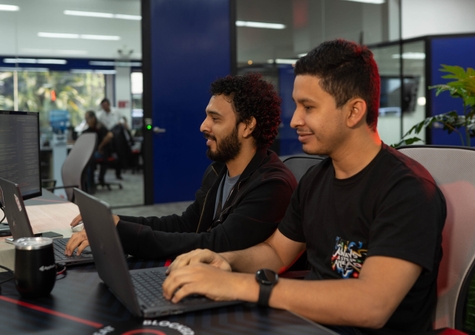 Two cloud expert professionals at a desk with laptops, collaborating on a project, showcasing an office like environment.