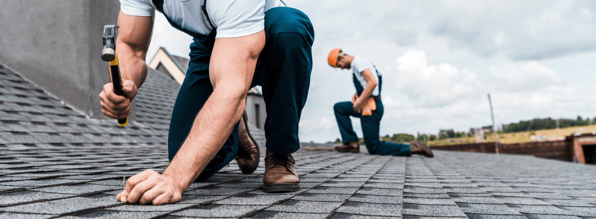 Two roofing professionals using tools to work on a roof, focused on their task in a construction setting