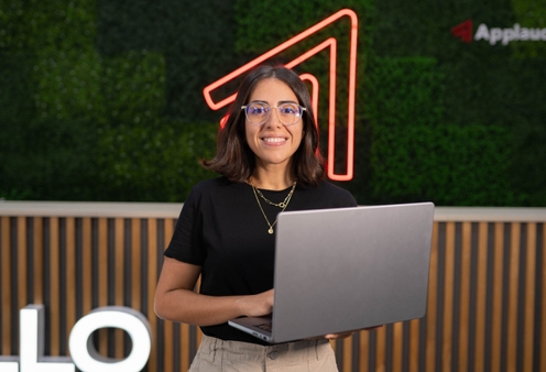 A female Applaudo employee holding a laptop and smiling to the camera