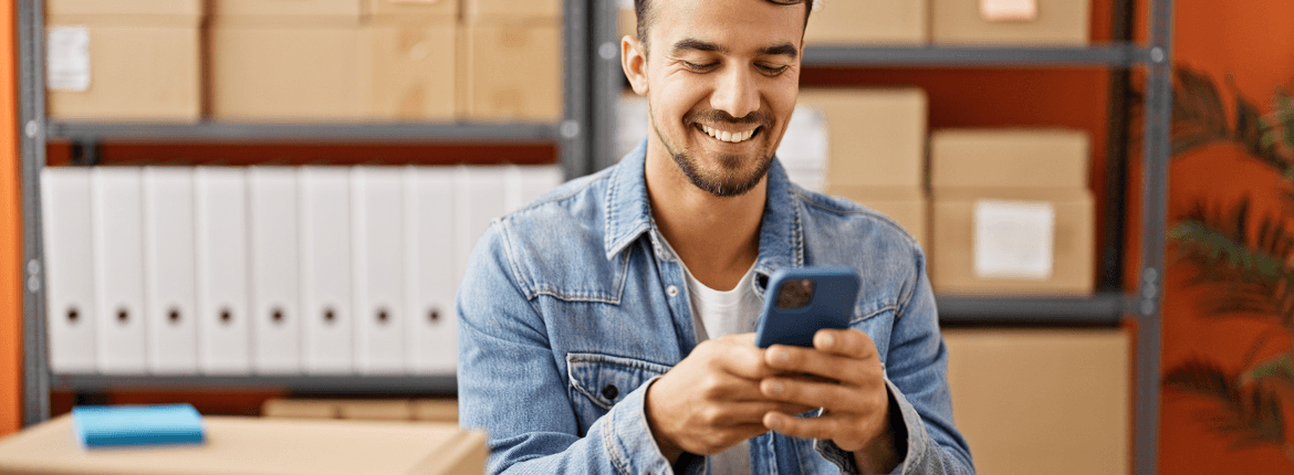 Male logistics worker reviewing finance data in a mobile phone in a warehouse.