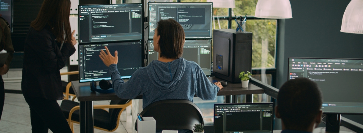 Male businessman reviewing code in a desktop computer with four monitors in an office